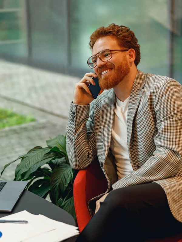 Smiling male boss talking phone with client while sitting in coworking space and working on