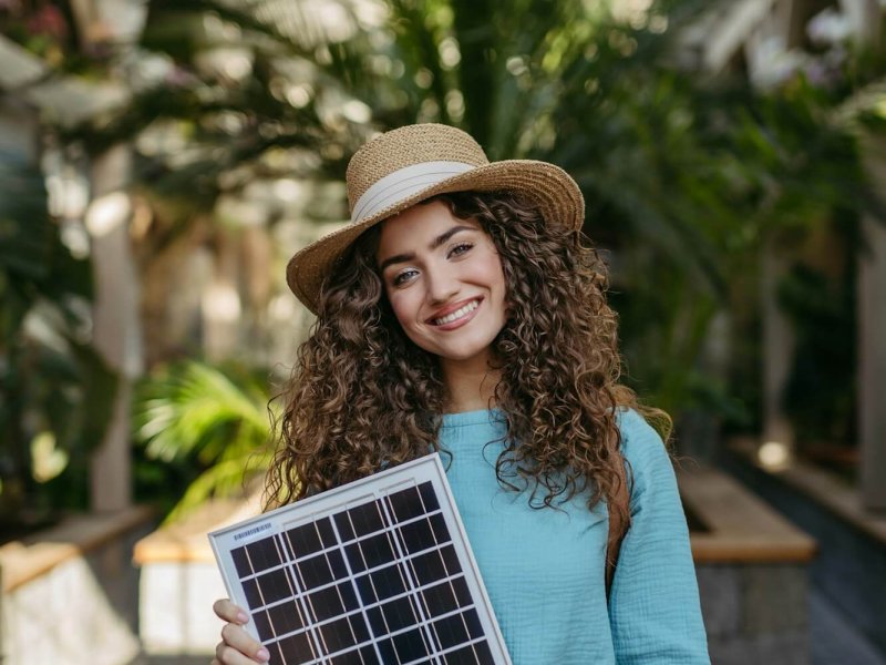 Young woman in botanical garden holding solar panel, concept of green energy.