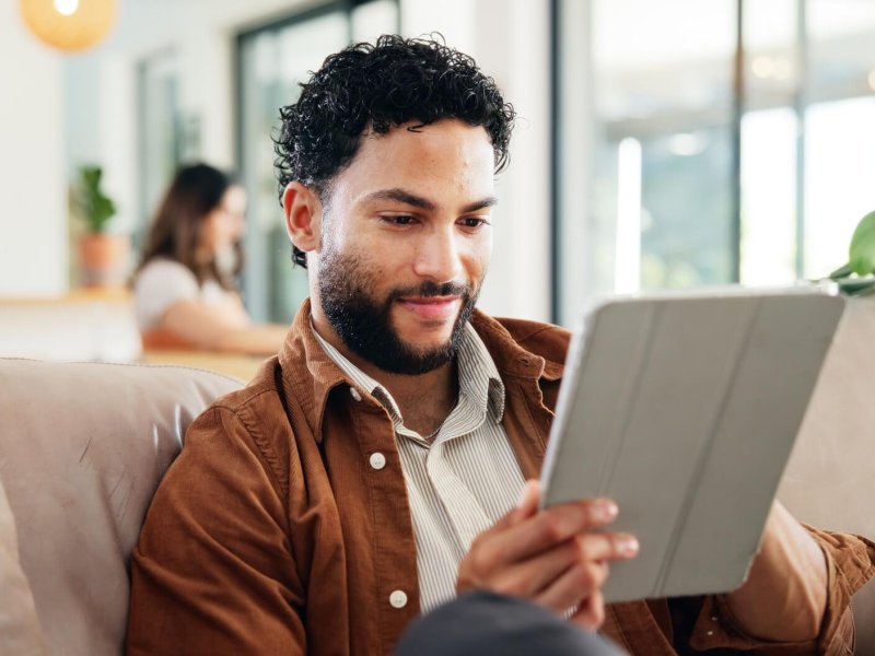 Man, relax and smile on sofa with tablet, social media and research for new home improvement. Perso