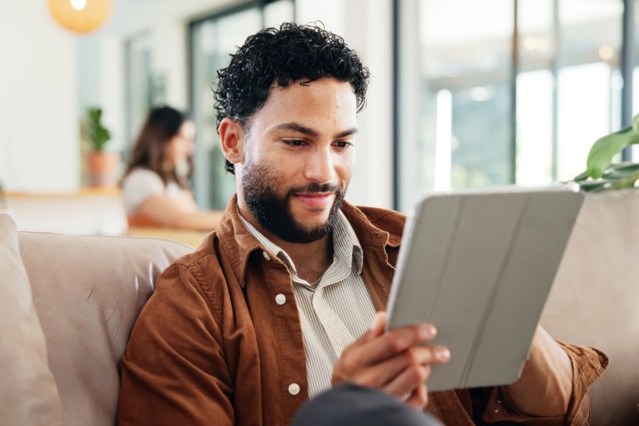 Man, relax and smile on sofa with tablet, social media and research for new home improvement. Perso