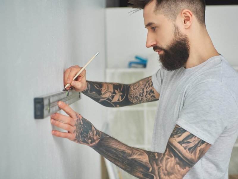 side view of handsome bearded young man holding level tool and pencil during home improvement