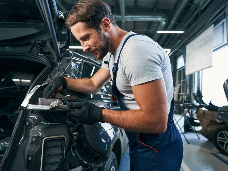 pleased-automotive-repairman-flattening-component-part-of-car