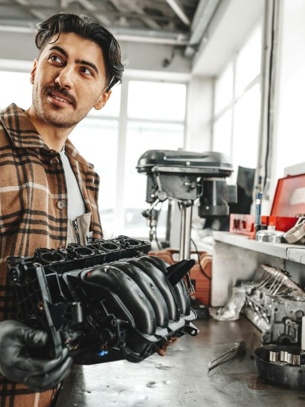 young-man-mechanic-repairing-car-parts-on-worktable-in-car-service-shop