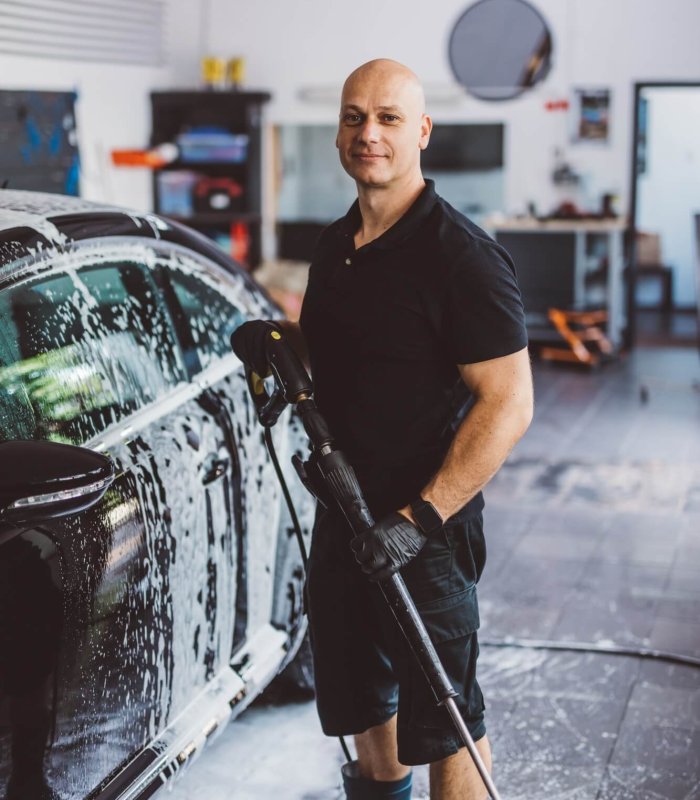 Service man washing car before detailing in workshop.