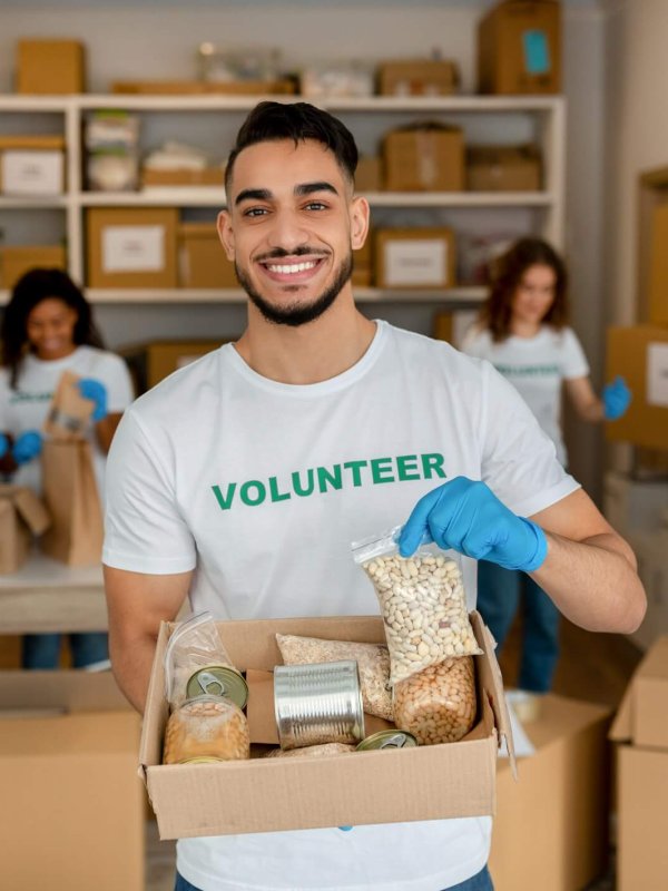 Young arab volunteer working at charity center, holding food donation box and smiling to camera
