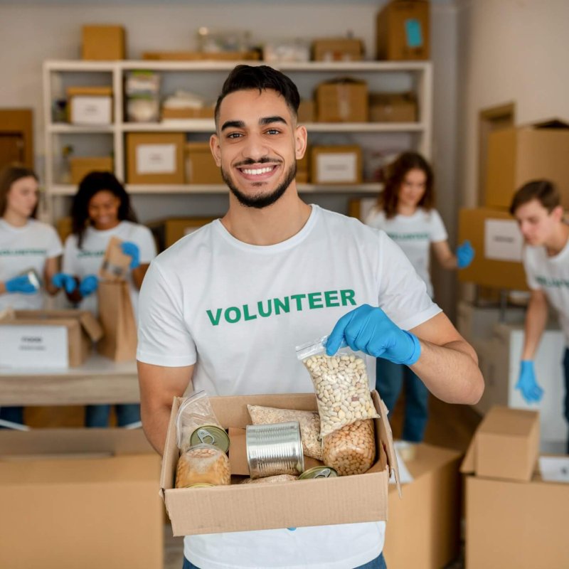 Young arab volunteer working at charity center, holding food donation box and smiling to camera